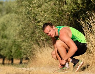 a man squatting down in a field with trees in the background