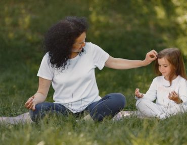 Mother and daughter bonding through yoga outdoors in a serene grassy field.